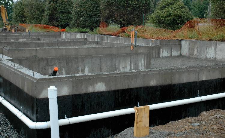 A man in an orange shirt is standing next to a wall.