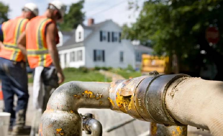 A man in an orange vest standing next to a pipe.